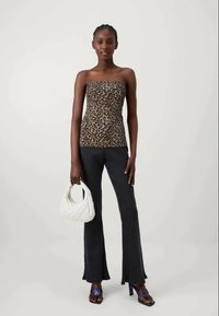 Top senza spalline con motivo leopardato, design aderente, abbinato a pantaloni scampanati scuri. Gli accessori includono una borsa a mano bianca e sandali blu.