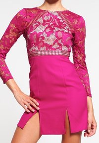Fuchsiové šaty s dlouhými krajkovými rukávy a krajkovým živůtkem, přičemž mají přiléhavou sukni a dva rozparky na stehnech pro moderní siluetu.