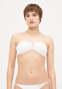 Hvit bikini topp med rynket design og tynne stropper. Materialet ser glatt og strukturert ut. Gulldetalj nær bunnen.