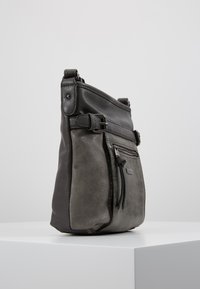 Sac à main en cuir gris avec une finition texturée, doté de bretelles ajustables, d'une poche frontale zippée et d'un design épuré et moderne.