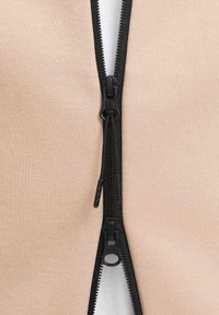 Giacca beige con zip, caratterizzata da una cerniera nera, tessuto testurizzato e una fodera interna liscia. La cerniera è posizionata centralmente sul davanti.