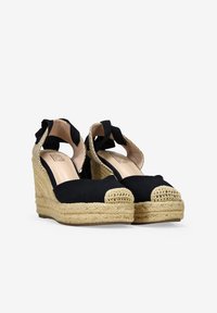Espadrilles noires à semelles en jute tressé, à bout rond et à dos ouvert. Présentent une sangle en tissu avec un accent nœud. Doublure intérieure lisse.