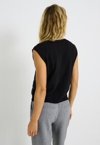 Haut sans manches noir avec un dos texturé, associé à un pantalon tailleur gris clair. Design simple, matériau doux, silhouette ajustée.