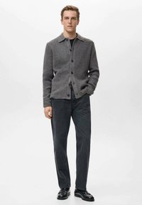 Szary sweter rozpinany z kołnierzem i guzikami, zestawiony z ciemnymi dżinsami i czarnymi butami, prezentowany na neutralnym tle.