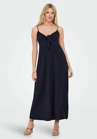 Robe maxi marine avec des bretelles spaghetti, un détail de nœud à l'avant et une silhouette fluide. Fabriquée en tissu léger avec une texture lisse.
