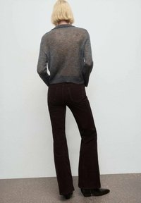 Suéter gris de punto transparente con mangas largas, combinado con pantalones de campana de burdeos oscuro. Botines negros completan el atuendo.