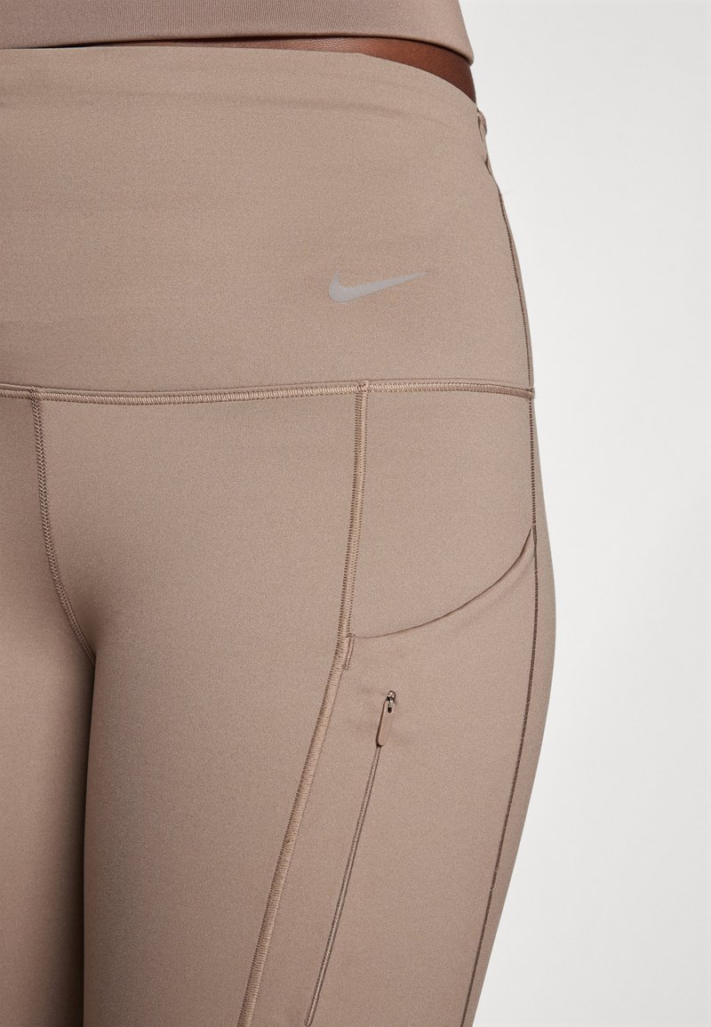 Beige sportleggings gemaakt van rekbaar materiaal, met een strak design, een subtiele Nike-logo en een ritszak aan de zijkant.