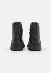 Crne čizme do gležnja od kože, s teksturiranim završetkom, ravnim potplatima i okruglim logom na peti. Uključene su dvije stražnje trake.