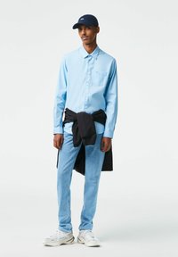 Camicia a maniche lunghe azzurri chiaro con chiusura a bottoni, taschino sul petto; maglione nero legato in vita; jeans azzurri chiaro; sneakers bianche.