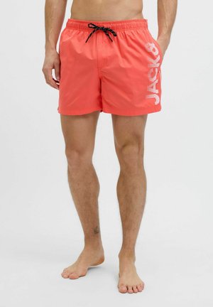 Bañador de coral con cinturilla elástica, cordón negro y diseño de logo blanco. El material es ligero y suave, ideal para el uso acuático.
