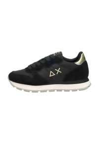 Zapatillas deportivas negras con una textura suave y de ante, suela blanca, detalles en dorado y logo en el lateral. Vista lateral.