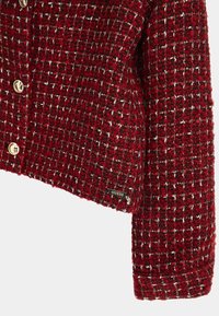 Blazer en tweed rouge avec un motif texturé, des boutons dorés et une petite étiquette 'Guess' près du poignet. Design court et ajusté.