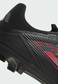 Chaussure de football noire avec une tige texturée, un design angulaire et des accents rouges. Comprend une forme épurée et une semelle extérieure noire détaillée.