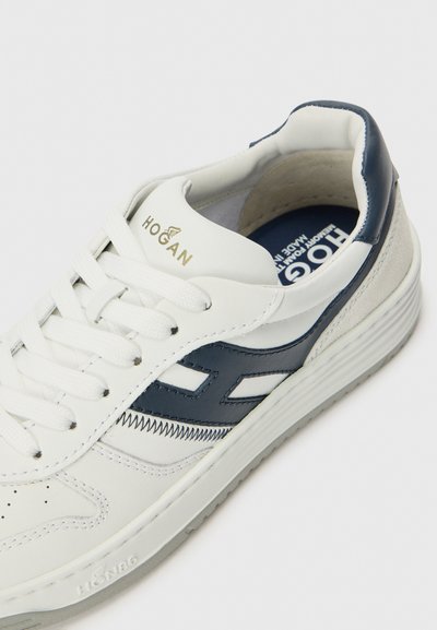 Sneakers bianchi in pelle con accenti blu navy, caratterizzati da un design testurizzato, lacci robusti e un collo imbottito. Logo dorato sulla linguetta.