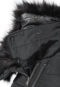 Collo del giubbotto invernale nero con bordo in pelliccia sintetica staccabile, bottoni a pressione e dettagli con zip a vista.