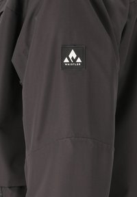 Zwarte jas met een gladde textuur, voorzien van een vierkant logo-embleem met de tekst "WHISTLER" en een bergafbeelding op de bovenste mouw.