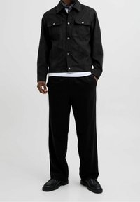 Czarna kurtka dżinsowa z dwoma kieszeniami na piersi, srebrnymi guzikami i dopasowanym krojem. W połączeniu z luźnymi czarnymi spodniami i czarnymi butami.