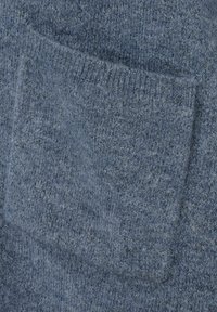 Blauwe gebreide stof met een close-up van een klein rechthoekig zakje dat op het materiaal is gestikt.