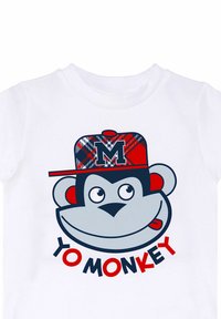 Hvid t-shirt med et tegneserieabe, der bærer en rød ternet kasket med et "M" logo og teksten "YO MONKEY" i fed rød skrifttype.
