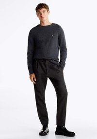 Maglione a maglia grigio scuro con polsini a coste, abbinato a pantaloni neri con trama e stivaletti neri alla caviglia. Design minimalista e forma aderente.