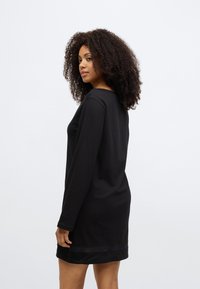 Črna obleka z dolgimi rokavi, okroglim izrezom in prosojnim robom. Iz mehkega materiala, ima sproščen kroj in minimalističen dizajn.