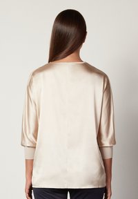 Satinbeige topp med trekvartslånga ärmar, rund halsringning, avslappnad passform och mjukt material. Minimalistisk design utan synliga mönster eller detaljer.