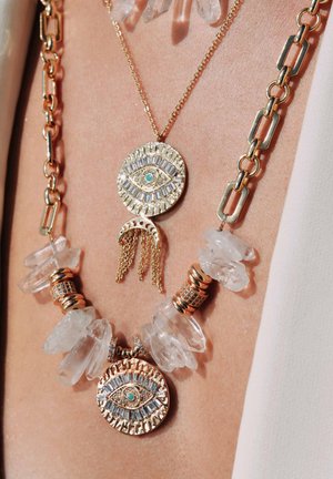 Gold-tone layered necklace featuring circular pendants with eye motifs, clear crystal accents, and textured metal links.