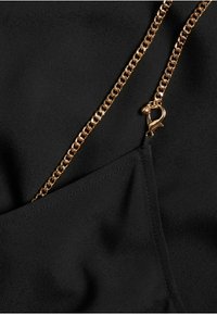 Schwarzer Stoff mit glatter Textur zeichnet sich durch einen goldenen Kettenriemen aus. Der Riemen hat ein Verschlussdetail und ist an einer Taschennaht befestigt.