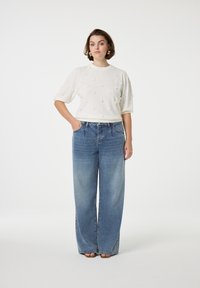 Creme gebreide top met textuuraccenten van bobbels, gecombineerd met lichtblauwe hoge taille, wijde jeans. Algemeen ontspannen silhouet.