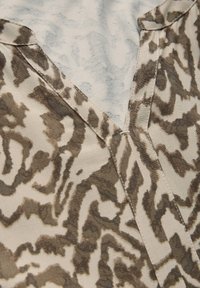 Beige und braun gemusterter Stoff mit V-Ausschnitt. Strukturierte Oberfläche mit abstrakten Designs. Nahtdetail entlang der Kanten.