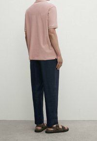 Polo rose clair, pantalon bleu marine foncé, sandales marron. Le polo présente un col standard, et la tenue est de coupe décontractée.