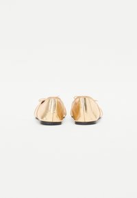Bailarinas metálicas doradas con superiores de tela suave, punteras redondeadas y detalles de lazo, con una textura suave y suelas planas.