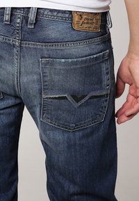 Vaqueros de mezclilla con un lavado azul oscuro, que cuentan con un diseño distintivo en el bolsillo trasero y una etiqueta de cuero de la marca en la cinturilla.