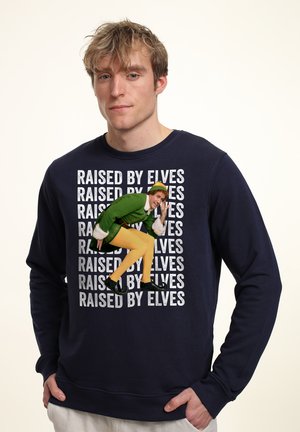 Marineblå sweatshirt med teksten "RAISED BY ELVES" i mønster. Frontgrafikken viser en karakter i et grønt outfit med gule bukser og sorte sko.