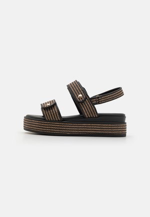 Plattformsandalen mit schwarzen synthetischen Riemen, ausgestattet mit zwei verstellbaren Schnallen, einem strukturierten gewebten Design und einer stabilen schwarzen Sohle.