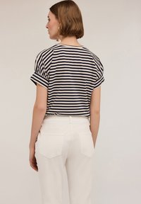 Striped short-sleeve top in navy and cream, with a relaxed fit. Paired with white high-waisted pants, showcasing back details and pockets.