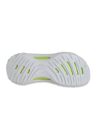 Semelle de chaussure en caoutchouc blanc avec un motif texturé, présentant des accents verts et des trous de ventilation pour une meilleure respiration. Le nom de la marque est visible.