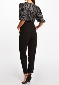 Svarta byxor med skräddarsydd passform och sidofickor, kombinerade med en mönstrad blus med puffärmar i svart och silver med blomsterdesign.