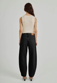 Svarta vida jeans med hög midja, tillverkade av denim. Bakpartiet har två fickor och en brun läderetikett vid midjan.