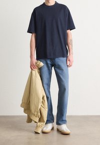 Marinblå bomullsoversized t-shirt kombinerad med ljusblå denimjeans. Håller en beige bomberjacka, vita skor med gummisålar. Enkel design.