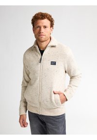 Beżowy sweter z zamkiem i teksturowanym splotem, z prążkowanym kołnierzem i mankietami. Posiada naszywkę z logo na lewej piersi oraz dwie boczne kieszenie.