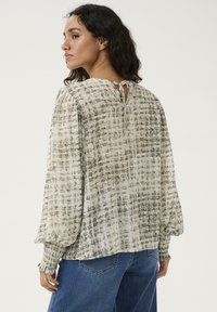 Blouse légère à motifs en blanc cassé et gris, présentant un dos en keyhole, des poignets smockés et une coupe décontractée avec des manches amples.