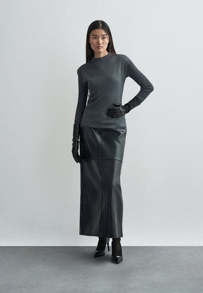 Fekete, enyhén fénylő, hosszú ujjú felső, amely egy fekete bőrnadrággal és szűk fekete kesztyűvel van párosítva, semleges háttér előtt.