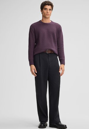 Maglione viola lavorato a maglia con finitura testurizzata, abbinato a pantaloni neri con vestibilità ampia e scarpe in pelle nera. La cintura marrone conferisce un contrasto.
