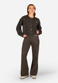 Tmavo šedý flísový kardigán s okrúhlym výstrihom, zapínaním na gombíky a dvoma prednými vreckami, spojený s rovnako farebnými širokými flísovými nohavicami.