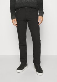 Musta slim-fit farkut, joissa on sileä pinta, viisi taskua ja nappikiinnitys, yhdistettynä mustiin tennareihin, joissa on valkoiset pohjat.