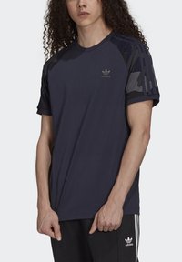 Marineblaue Sport-T-Shirt mit rundem Halsausschnitt, Raglanärmeln und dunklen Camouflage-muster Akzenten. Aus atmungsaktivem Material mit Logodetail gefertigt.