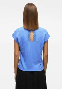 Niebieski krótki top z krótkimi rękawami wykonany z teksturowanej tkaniny, z wycięciem w kształcie klucza wykończonym koronką na plecach. Gładkie wykończenie i casualowy krój.