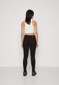 Jeans elásticos negros con cintura alta, diseño ajustado y dos bolsillos traseros, combinados con una camiseta sin mangas cortada blanca y zapatillas negras.
