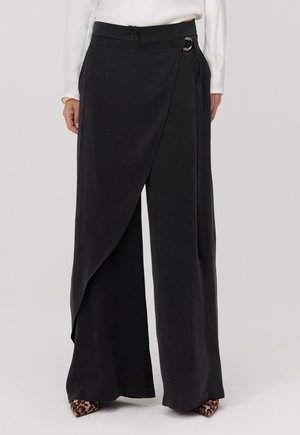 Czarne spodnie o szerokich nogawkach z kopertowym fasonem, zapinane na boczny guzik, wykonane z gładkiej, teksturowanej tkaniny. Charakterystyczne układanie i wykończenie u dołu nogawek.